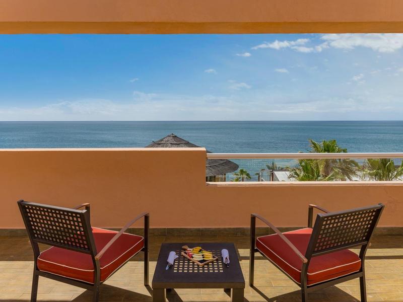 Terrassenblick auf das Meer mit zwei roten Sesseln und einem kleinen Tisch dazwischen.