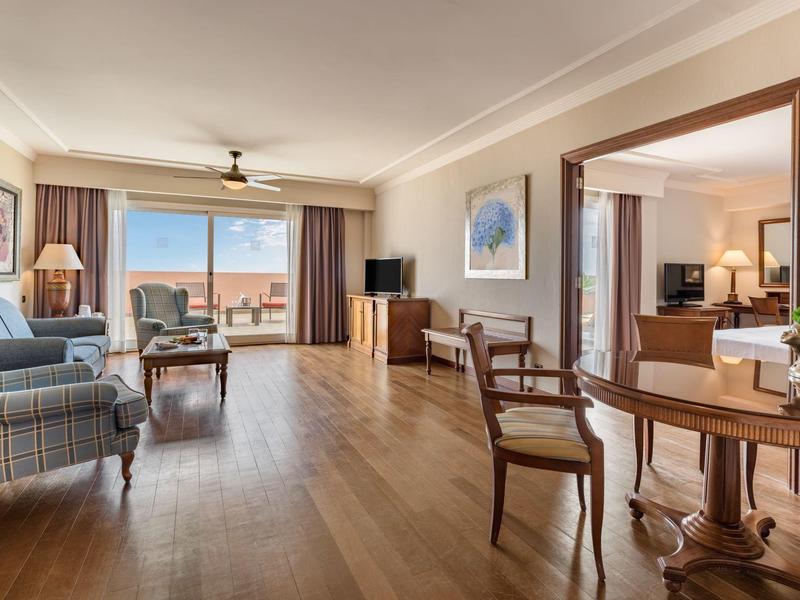 Geräumiges Wohnzimmer mit Holzboden, Sesseln, Tisch, Fernseher und großem Fenster mit Meeresblick.