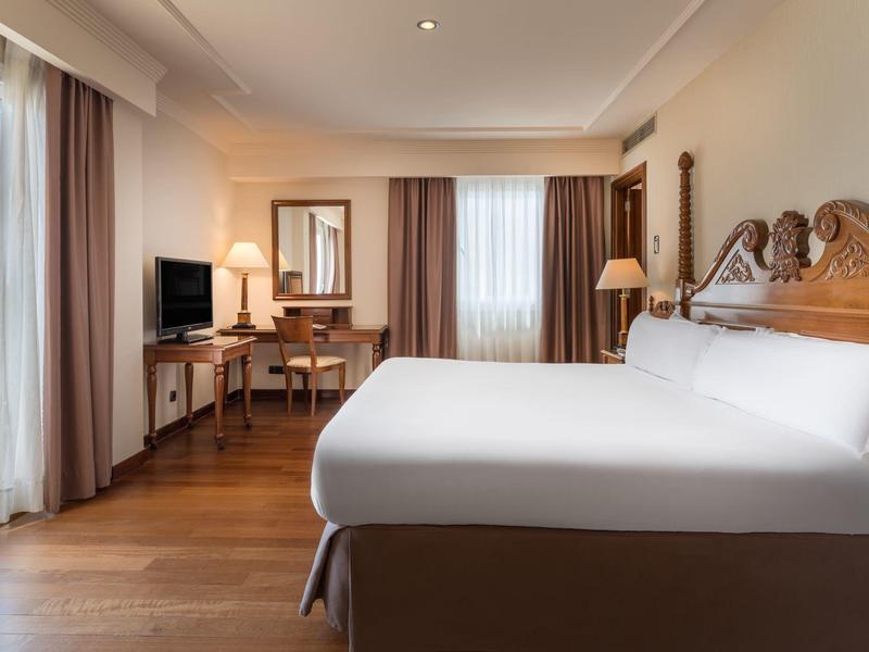 Hell eingerichtetes Schlafzimmer mit großem Bett, Holzfußboden, Fenster und Schreibtisch.