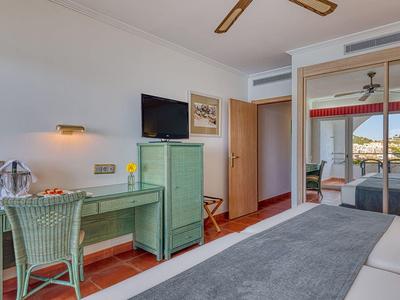 Helles Hotelzimmer mit grünem Schreibtisch, Stuhl, TV, Spiegel-Schrank und Blick aufs Meer.