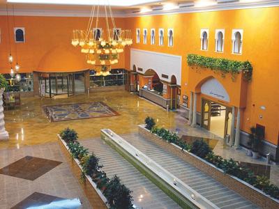 Großer, heller Innenraum mit orangen Wänden, Wasserspiel, Pflanzen und Kronleuchtern, elegant gestaltet.