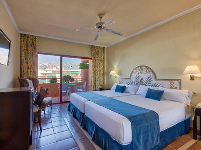 Gemütliches Hotelzimmer mit zwei Einzelbetten, Balkon, Ventilator und sonniger Aussicht.