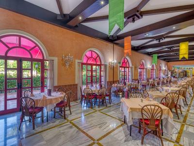 Großer, heller Gastraum mit rosa Fensterbögen, Holztischen, Stühlen und bunten Wimpeln an der Decke.