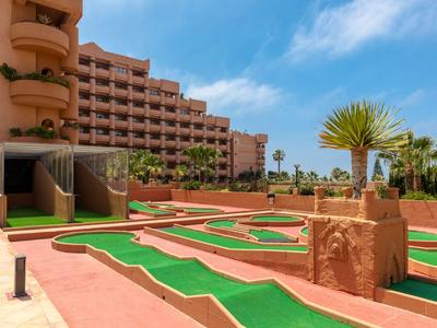 Minigolfplatz vor einem mehrstöckigen Hotelgebäude unter blauem Himmel.