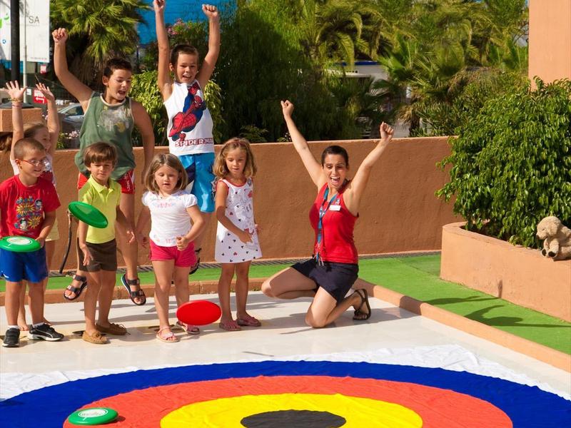Gruppe glücklicher Kinder und Erwachsene springt neben einem bunten Bogenschießziel auf einer Terrasse.