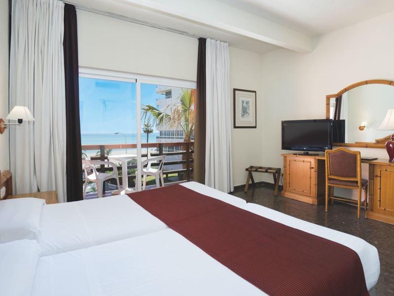 Helles Schlafzimmer mit Doppelbett, braunen Akzenten und Balkon mit Meeresblick.