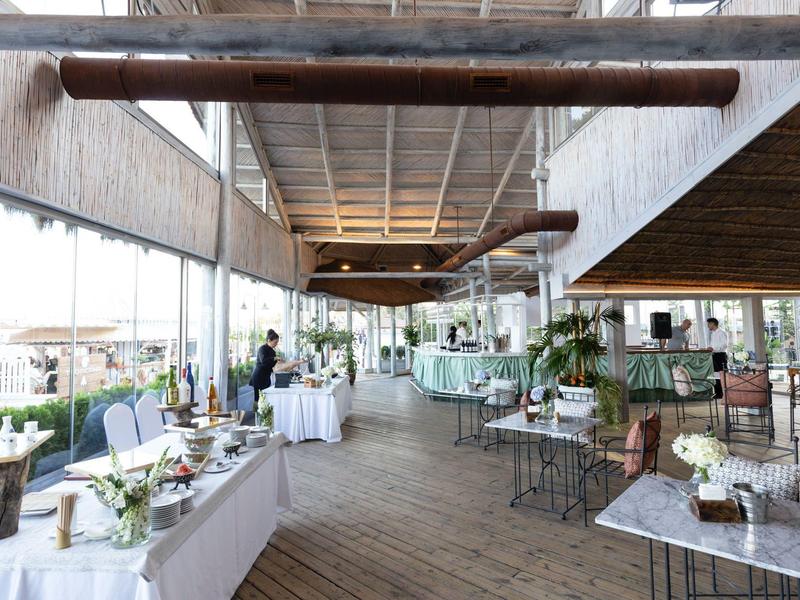 Großer heller Gastraum mit Holzboden, großen Fenstern, weißen Tischen und moderner Dekoration.