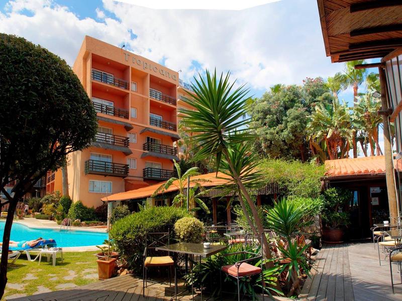 Garten mit Pool, Palmen und Sitzbereich vor orangefarbenem Wohnhaus unter blauem Himmel.