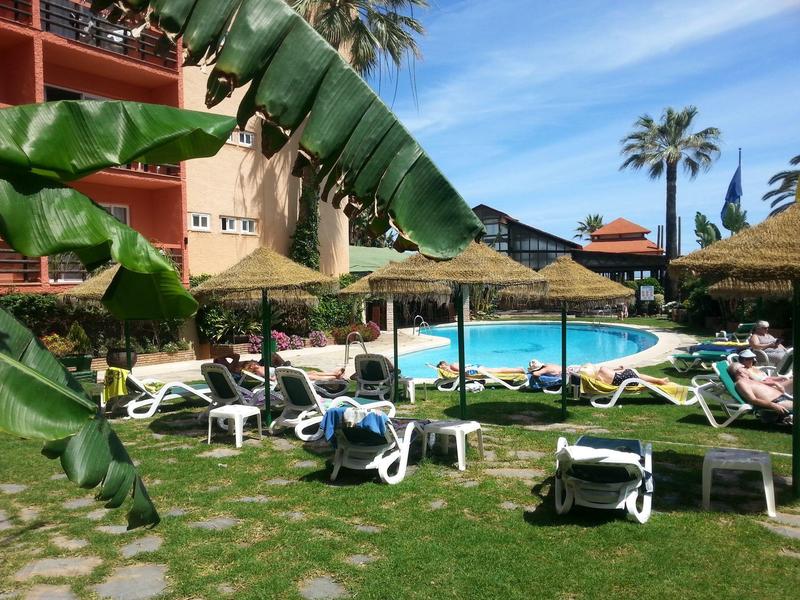 Ein Poolbereich mit weißen Liegestühlen, Strohdächern und großen grünen Bananenblättern.