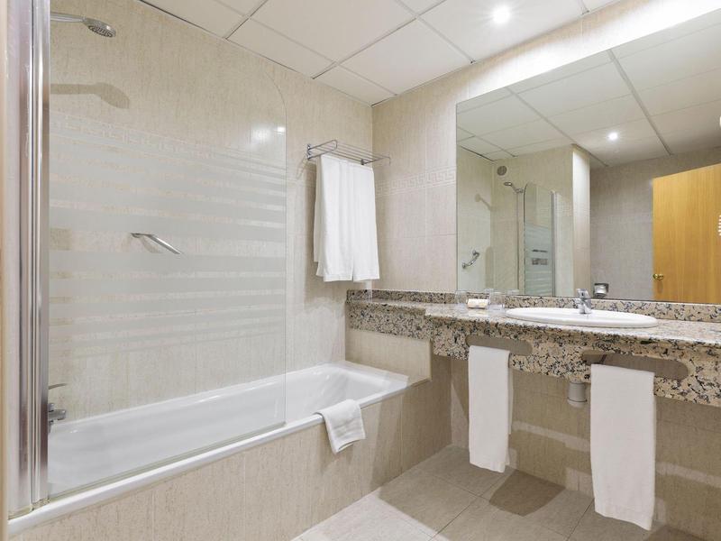 Helles Badezimmer mit Badewanne, großem Spiegel, Doppelwaschbecken und Handtüchern.