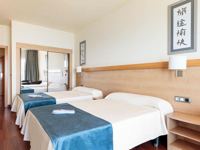 Hell eingerichtetes Doppelzimmer mit Holzboden, zwei Betten, blauen Bettläufern und großen Spiegeln.