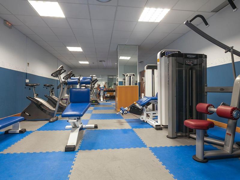 Kleines Fitnessstudio mit blauen Mattenboden, Kraftgeräten und Fahrradergometern in einem hellen Raum.