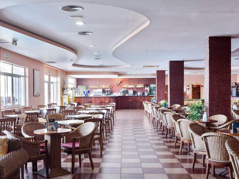 Großer heller Gastraum mit Holz- und geflochtenen Stühlen, runder Decke und Theke im Hintergrund.