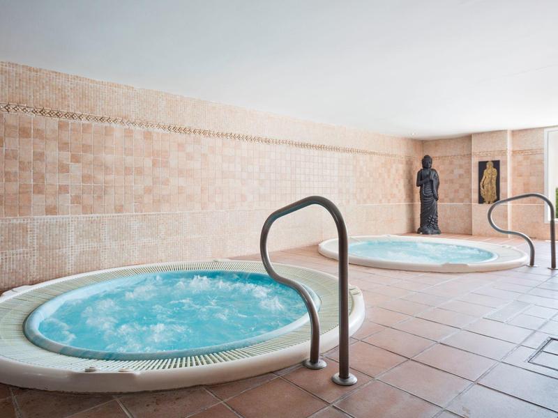 Innenraum mit zwei runden Whirlpools, helle Steinwände und großer Fenster mit Blick ins Grüne.