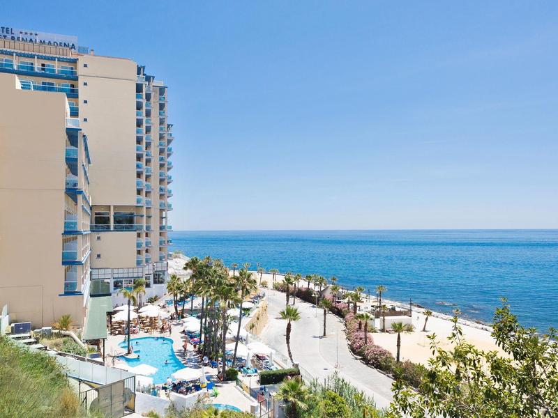 Hochhaus am Meer mit Pool, Spazierweg, Palmen und blauem Himmel an der Küste.