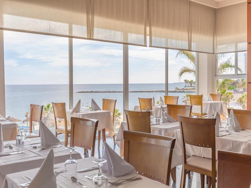 Elegantes Restaurant mit weißen Tischdecken und großem Fenster mit Blick aufs Meer.