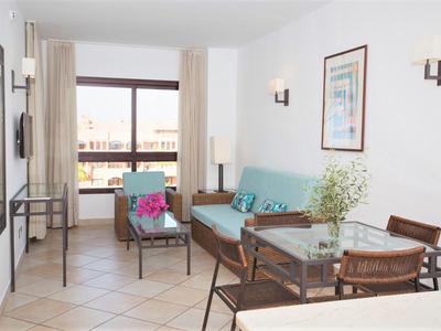 Helles Wohnzimmer mit Sofa, Glastisch, Stühlen und großem Fenster mit Blick auf Balkon.