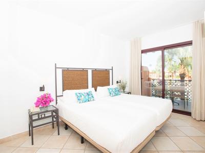 Helles Schlafzimmer mit Doppelbett, weißen Wänden und Zugang zu Balkon mit Gartenblick.