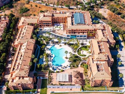 Luftaufnahme eines großen Hotels mit Innenhof und mehreren Pools, umgeben von Bäumen und Straßen.