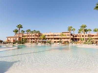 Großer Hotelpool mit Palmen und mehrstöckigem Gebäude unter klarem Himmel