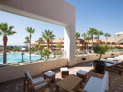 Blick auf einen Poolbereich mit Palmen und Liegestühlen in einem Hotelresort bei sonnigem Wetter.