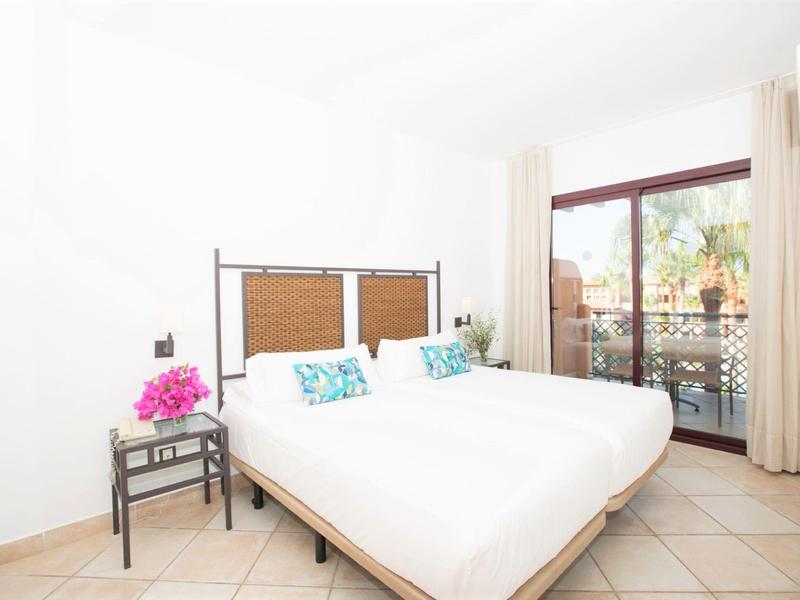 Helles Schlafzimmer mit Doppelbett, weißen Wänden und Zugang zu Balkon mit Gartenblick.