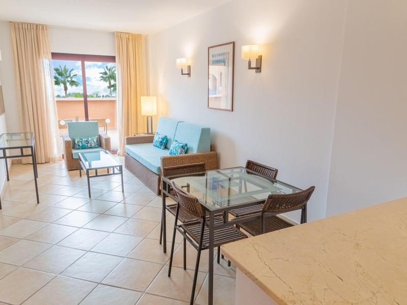 Heller Wohnraum mit Esstisch, Sofa und Blick auf Balkon mit Meerblick.