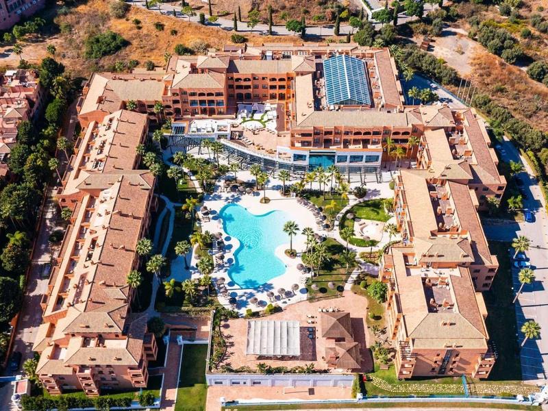 Luftaufnahme eines großen Hotels mit Innenhof und mehreren Pools, umgeben von Bäumen und Straßen.