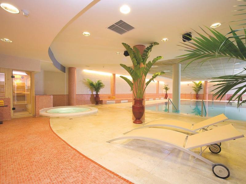 Innenpoolbereich mit Liegestühlen, Palmen und warmem Licht in einem Hotel.