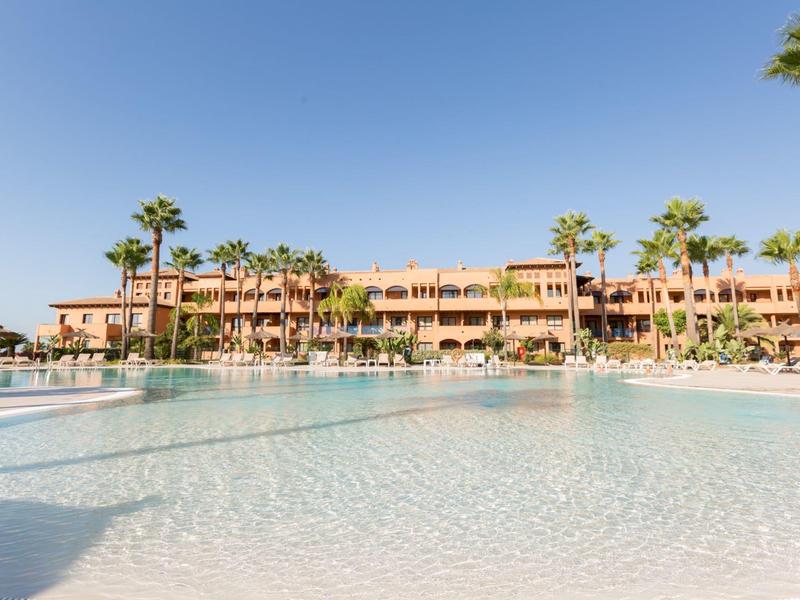 Großer Hotelpool mit Palmen und mehrstöckigem Gebäude unter klarem Himmel