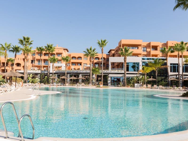 Großer Hotelpool mit Sonnenliegen und Palmen unter klarem Himmel