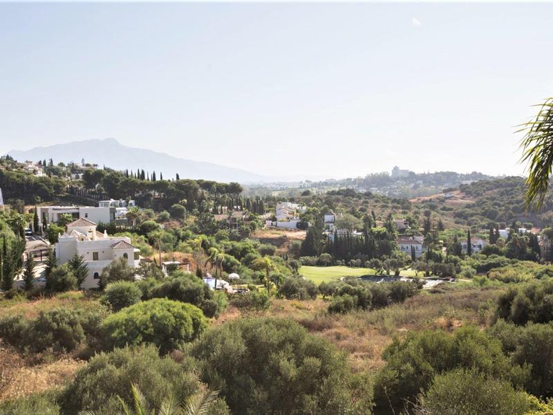 Landschaft mit grünen Hügeln, Häusern und Bergen im Hintergrund an einem klaren Tag
