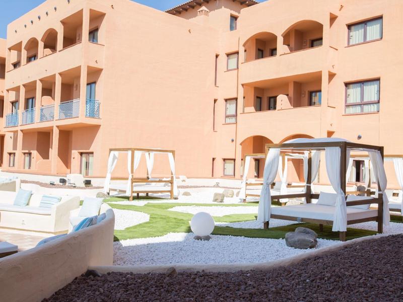 Hotelaußenbereich mit Poolliegen, Pavillons und Rasenflächen bei sonnigem Wetter.