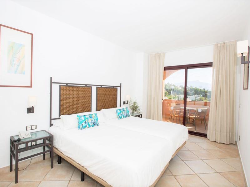 Helles Schlafzimmer mit Doppelbett, bunten Kissen und Balkonblick auf Berge und Meer.