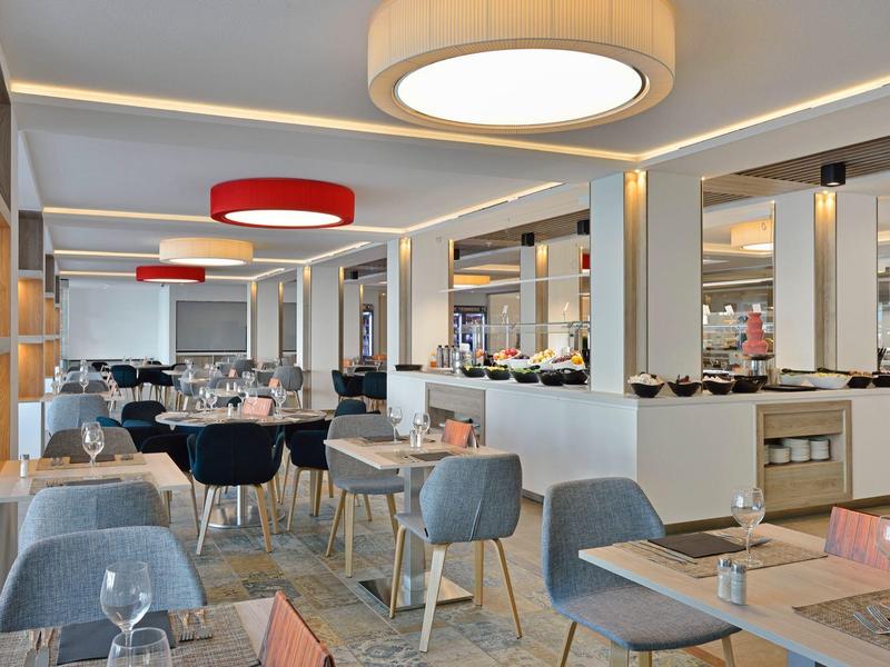 Modernes Restaurant mit grauen Stühlen, Holztischen, großen Spiegeln und runden Deckenleuchten.