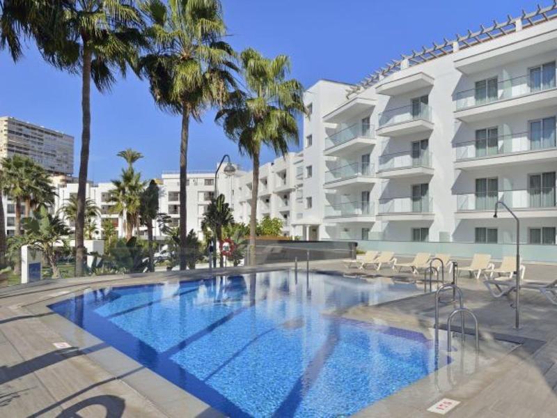 Moderner Poolbereich mit klar blauem Wasser, weißen Liegen und fünfstöckigem weißem Hotelgebäude.