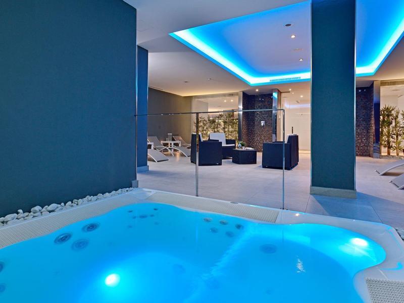 Moderner Wellnessbereich mit beleuchtetem Whirlpool, blauem Ambiente und gemütlichen Sitzmöbeln.