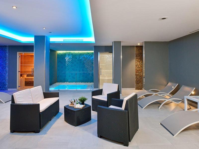 Moderner Wellnessbereich mit bequemen Sesseln, Liegen und blau beleuchtetem Pool.