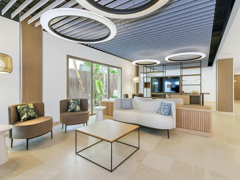 Heller, moderner Wohnraum mit weißem Sofa, zwei braunen Sesseln, runden Deckenleuchten und großem Fenster.