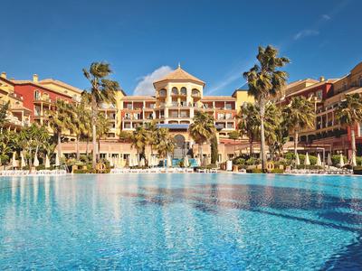 Großes Hotel mit Palmen und einem klaren blauen Pool unter klarem Himmel