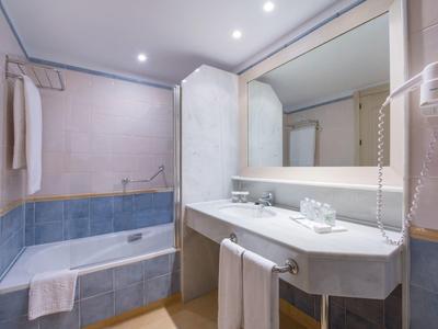 Sauberes Badezimmer mit Badewanne, großem Spiegel, Waschbecken und Handtüchern, weiß und blau gefliest.