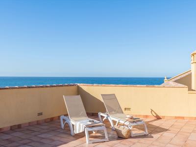 Zwei weiße Liegestühle auf einer sonnigen Dachterrasse mit Blick auf das blaue Meer.