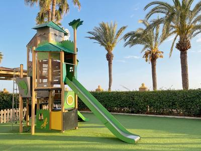 Area giochi per bambini con scivolo verde e torre, circondata da palme nel giardino dell'hotel.
