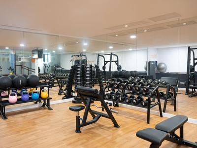 Palestra moderna con manubri, panche per allenamento e parete a specchio su pavimento in legno.