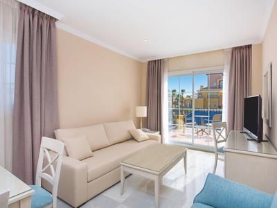 Helles Wohnzimmer mit beiger Couch, weißen Möbeln, blauem Sessel und großem Fenster mit Stadtblick.