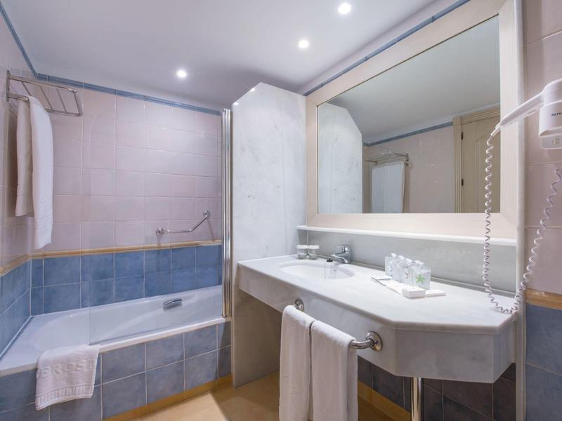 Sauberes Badezimmer mit Badewanne, großem Spiegel, Waschbecken und Handtüchern, weiß und blau gefliest.