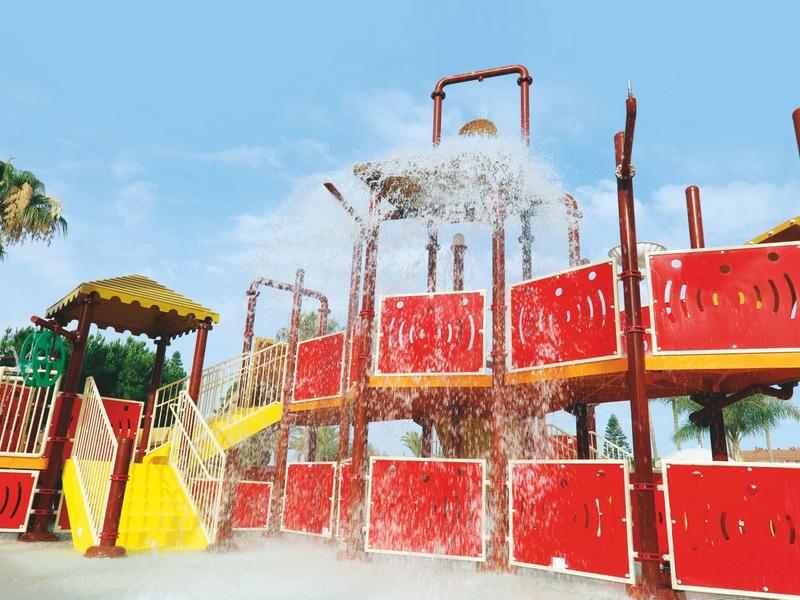 Bunter Wasserspielplatz mit roten, gelben und grünen Elementen unter blauem Himmel.