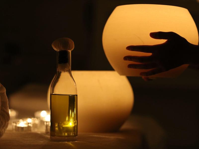 Eine Hand berührt eine orangefarbene Lampe, daneben steht eine kleine Glasflasche mit einem Korken.