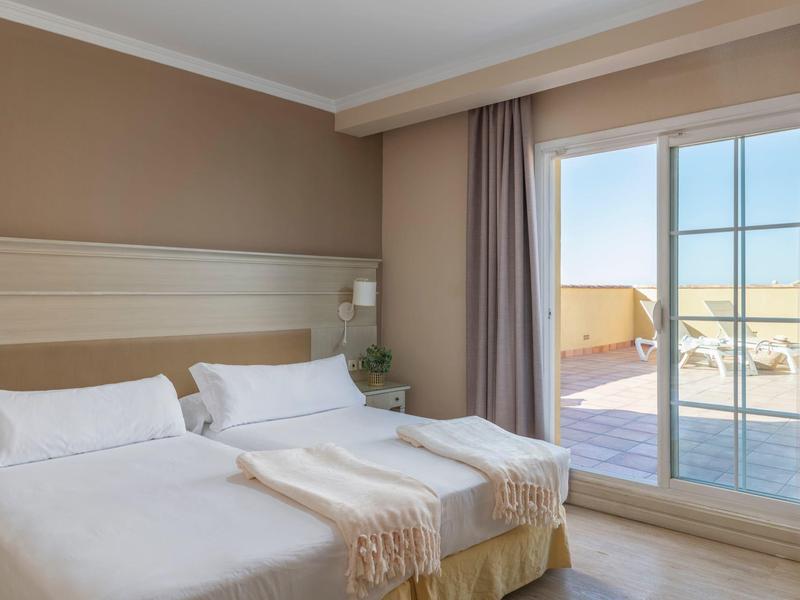 Hell eingerichtetes Schlafzimmer mit zwei Einzelbetten und großer Glasschiebetür zum Balkon.