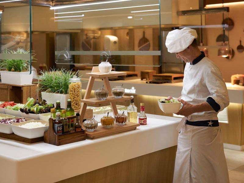 Koch in weißer Uniform bereitet Salat in moderner, gut beleuchteter Küche mit frischen Zutaten zu.